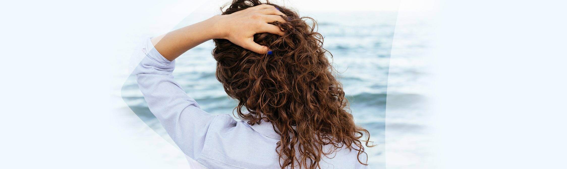 Une femme contemple la mer, les mains dans les cheveux