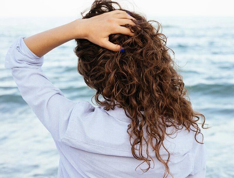 Vrouw met de handen in het haar kijkt over de zee uit
